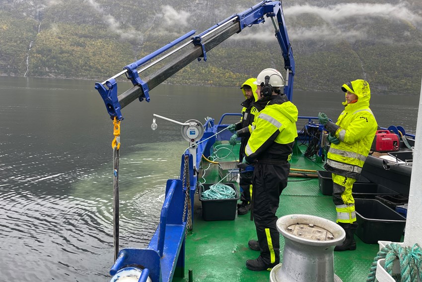 Arbeidsbåt og mannskap som jobber med prøvetaking i vann. Foto.