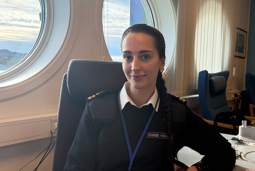 Ung kvinne i uniform sitter ved pult. Foto.