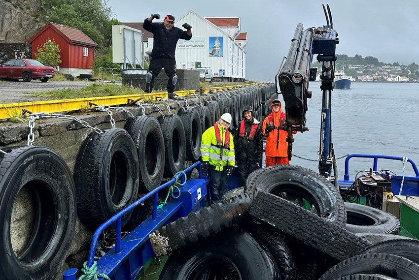 Kaifront med fenderdekk og båt med dekk samt ungdommer. Foto.